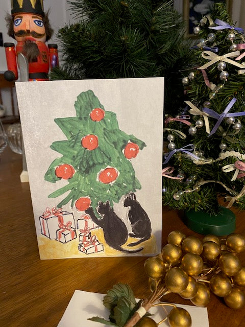 Hand-drawn card with a Christmas tree and cat on a wooden surface with holiday decorations.