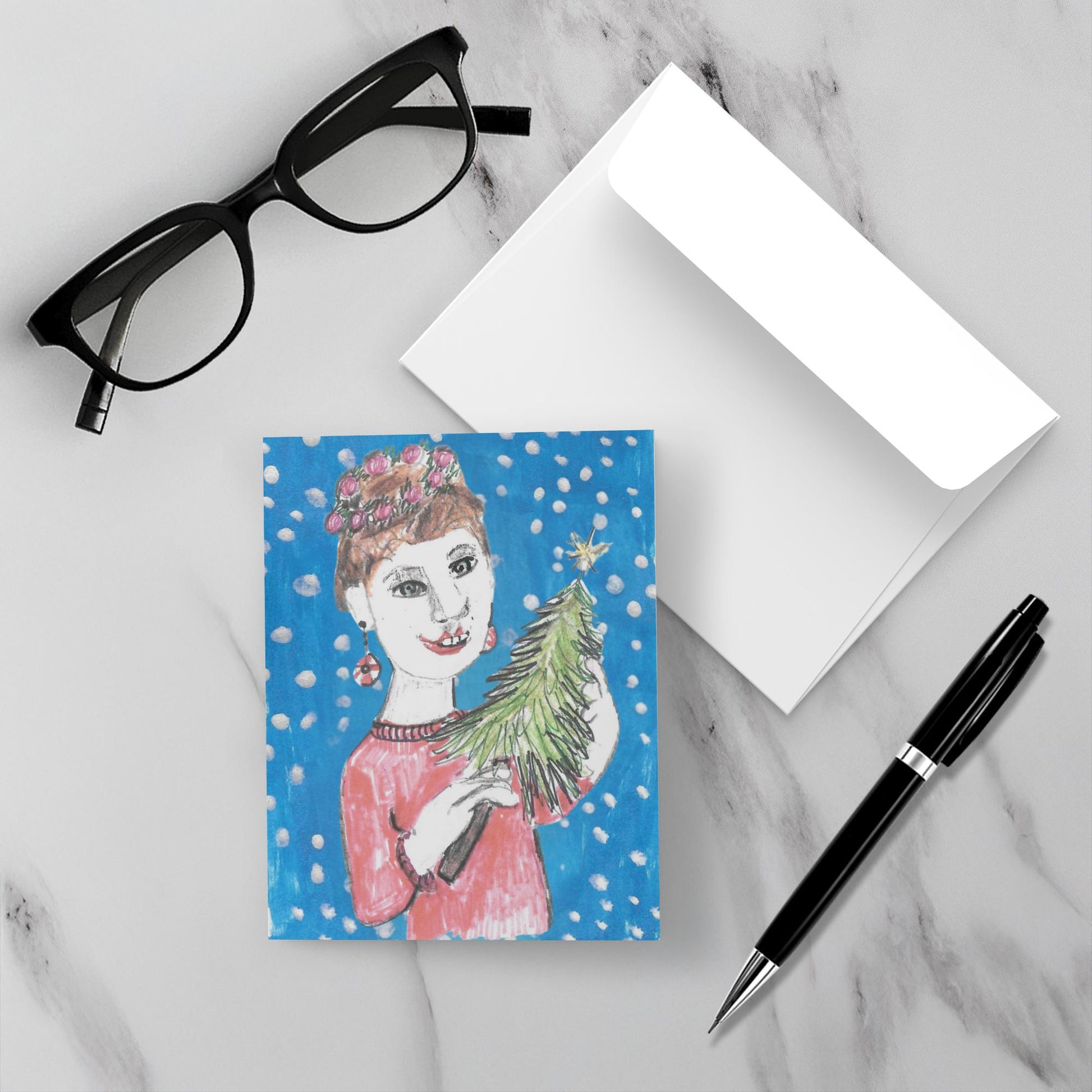 Greeting card with a woman holding a Christmas tree, glasses, pen, and envelope on a marble surface.