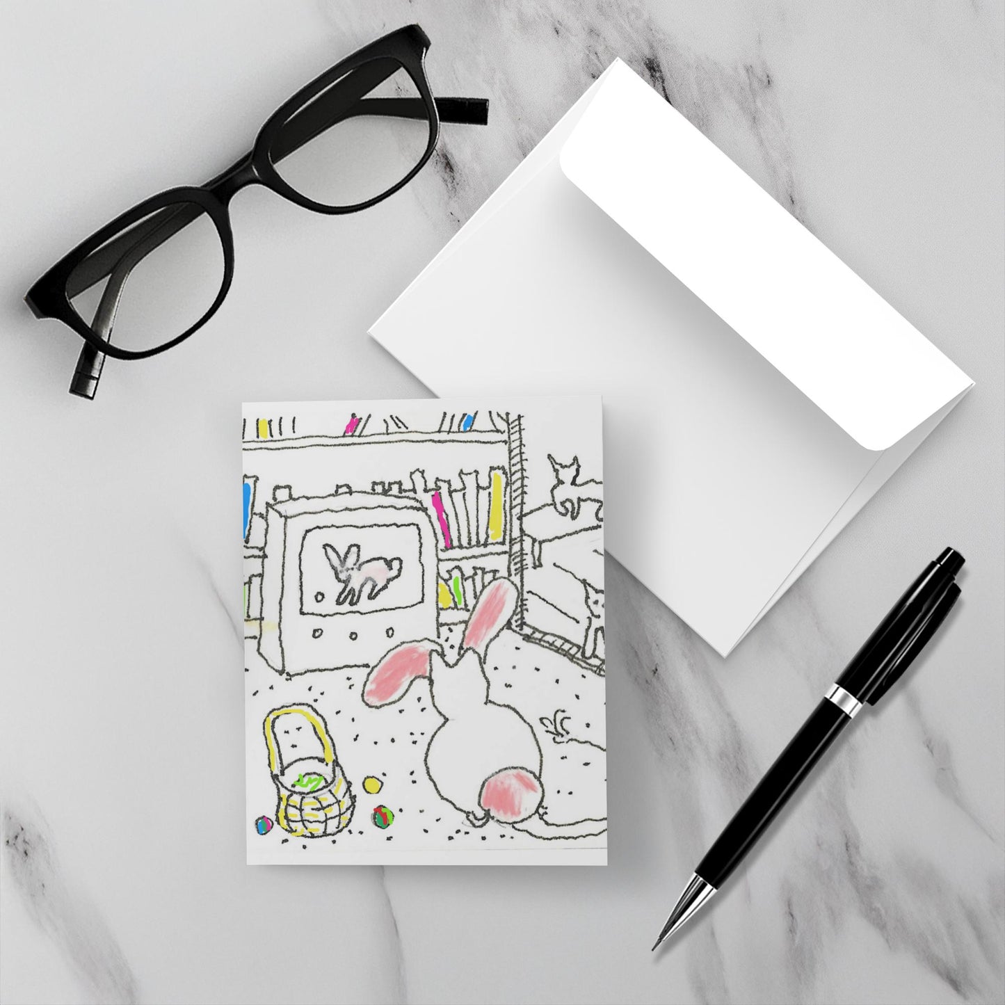 A mock up of the Easter card on a white marble background with the card on top of the envelope. A pen and reading glasses complete the picture.