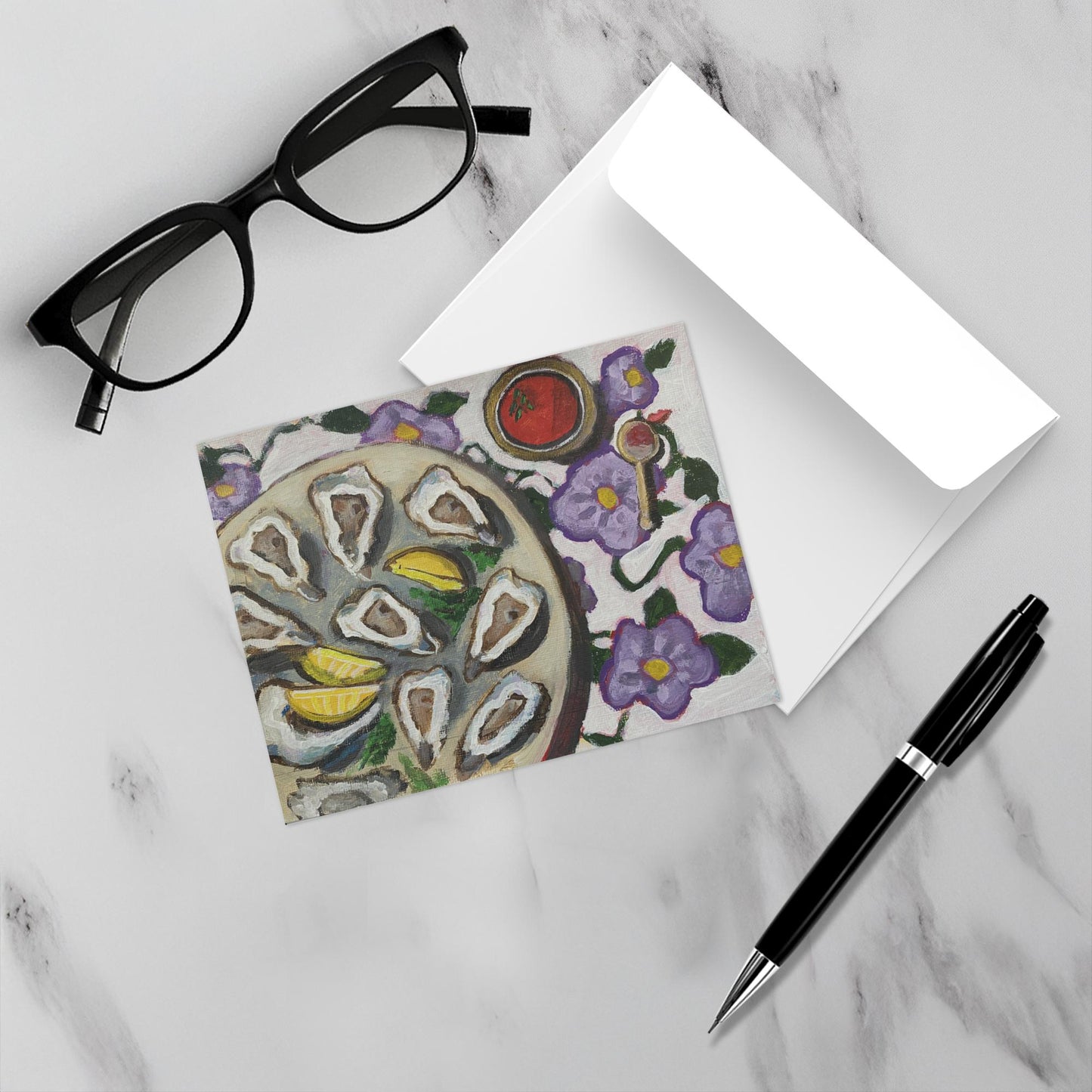 Oyster Sisters Social shown with its envelope a pen and eyewear on a white  marble surface.