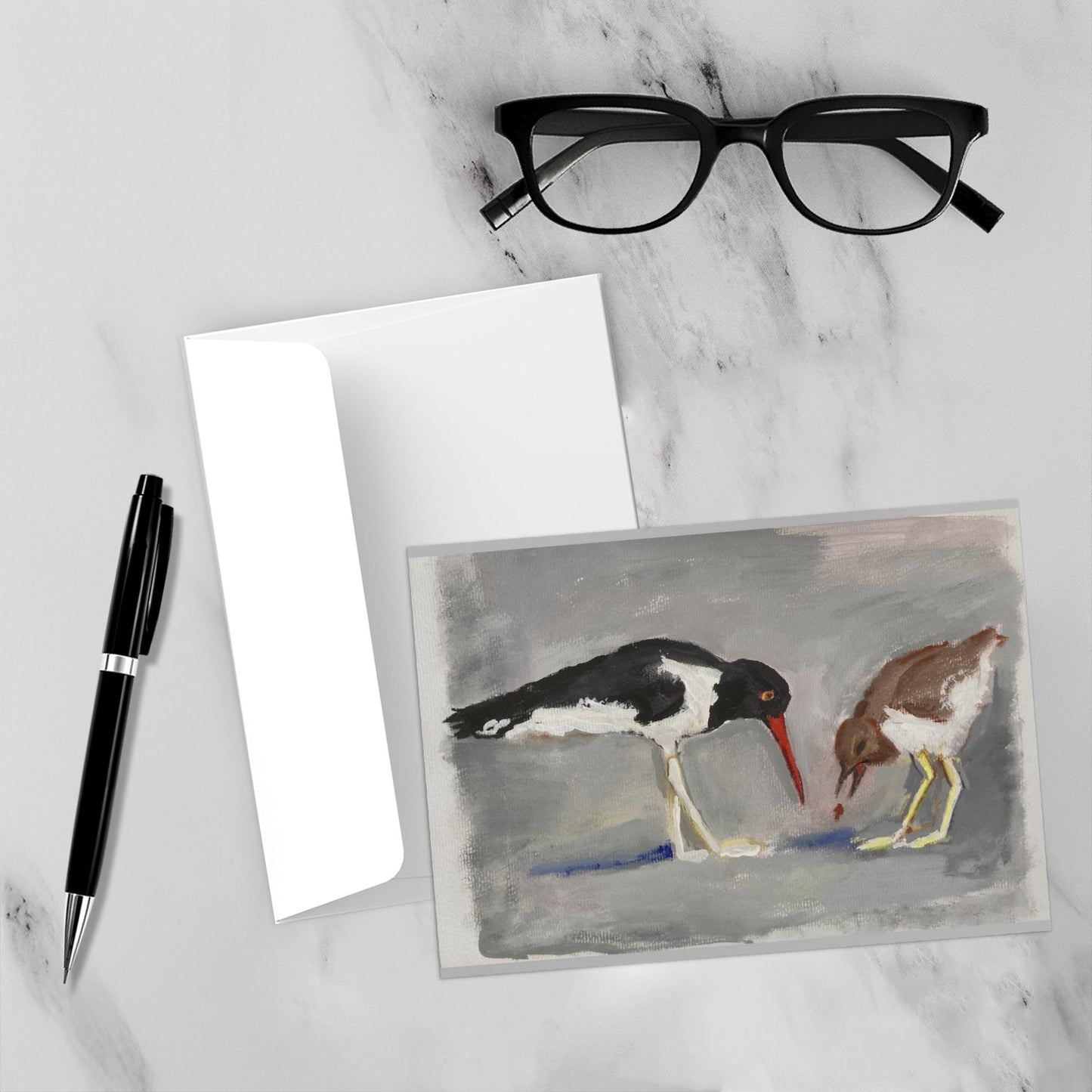 The Shore Birds are placed by the envelope on a white marble backdrop. A pen and reading glasses are nearby.