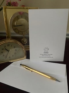 The back of the Card The Most Delicious Cake displayed on a desk with a white envelope and gold pen in the foreground and gold desk clocks on the left.