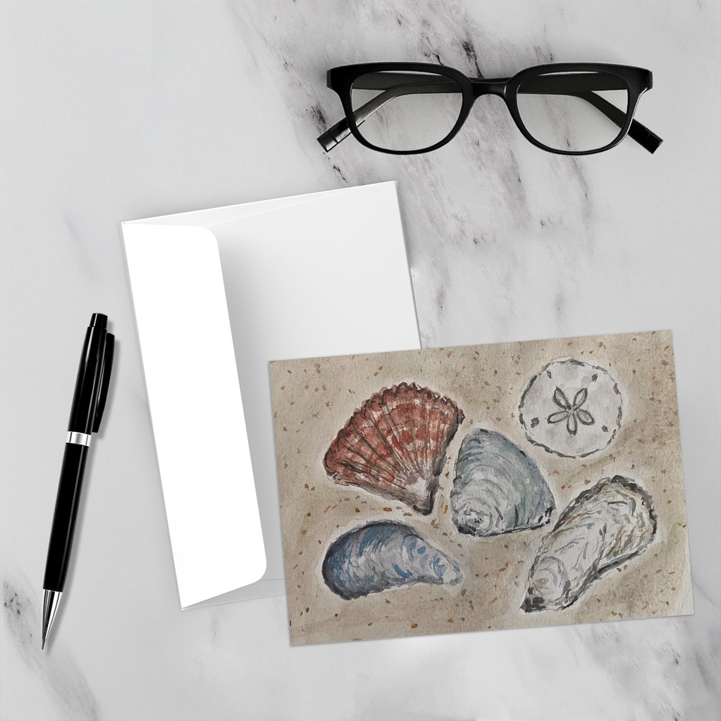 The seashells really pop against the white marble backdrop of this mockup. The envelope, a pen, and reading glasses are also featured.