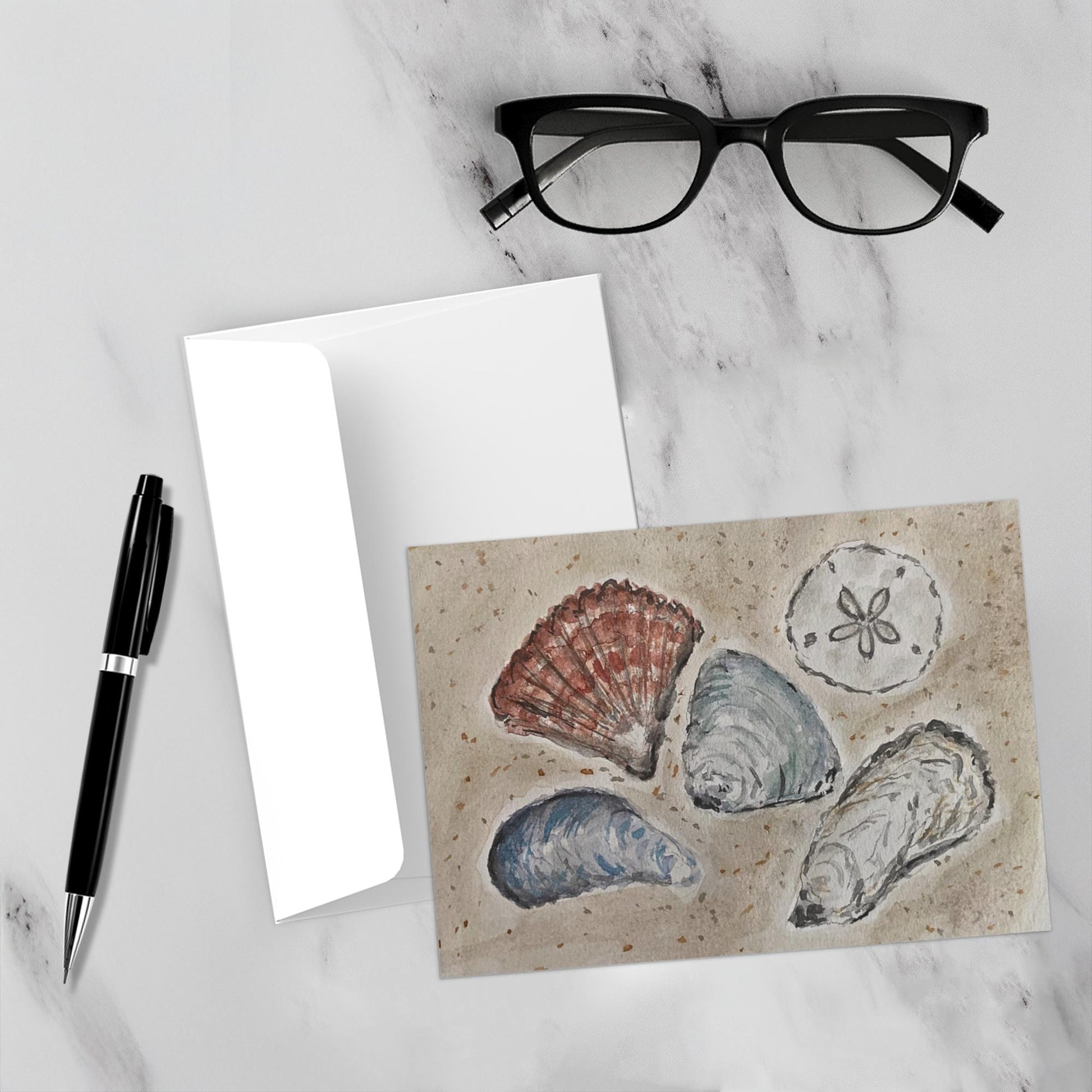 The seashells really pop against the white marble backdrop of this mockup. The envelope, a pen, and reading glasses are also featured.