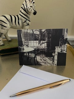 The front of the photo greeting card Vermont Light is displayed on a gold colored tray with a white envelope and a gold pen in the foreground and a statue of a black and white zebra in the background.