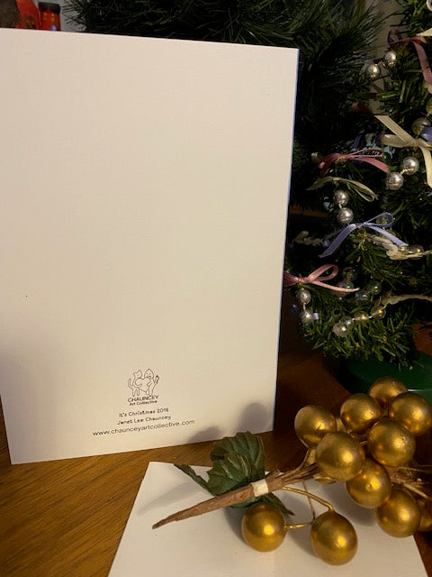 The back of the greeting card with Chauncey Art Collective logo on a wooden table with holiday decorations.