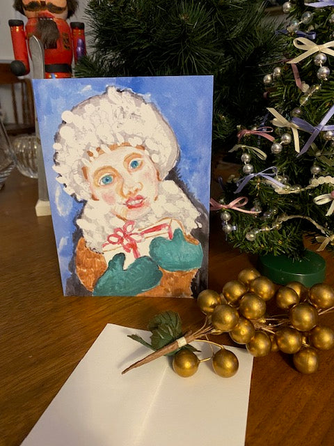 Christmas card It's Christmas by Janet Lee Chauncey shows a girl in a white hat holding a gift with green mittens.