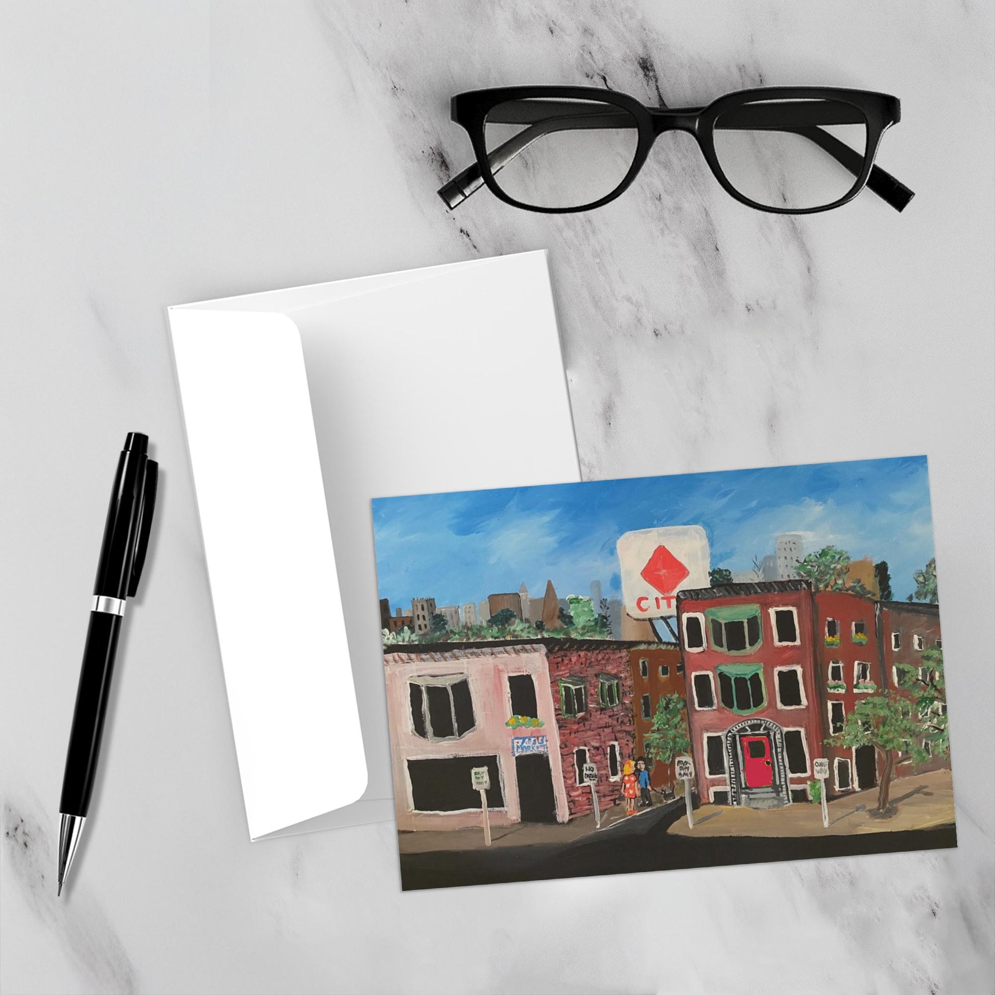 The colorful card is placed face up on a marble backdrop with the envelope, a pen and reading glasses nearby.